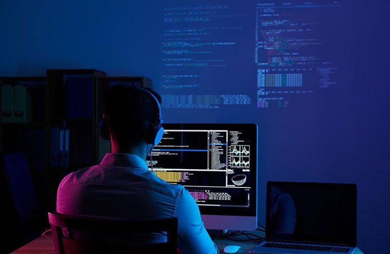 Software developer wearing headphones and reviewing code on a large flat screen monitor